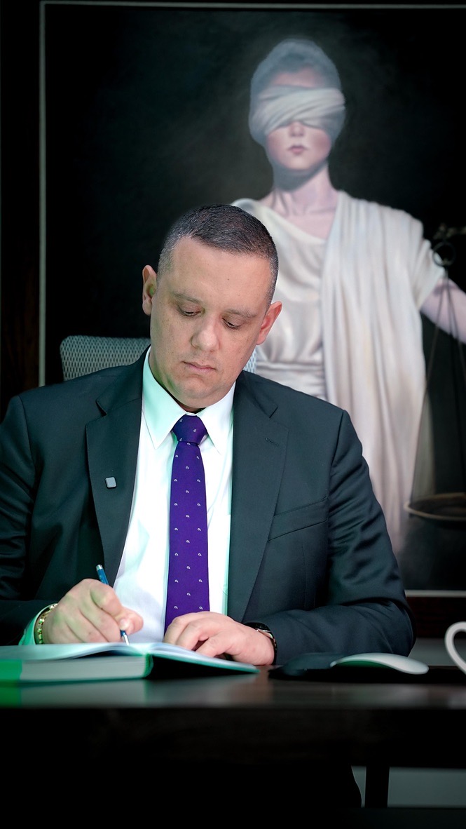El abogado Ricardo Andrés Giraldo Cifuentes firmando un documento, frente a un retrato de la justicia